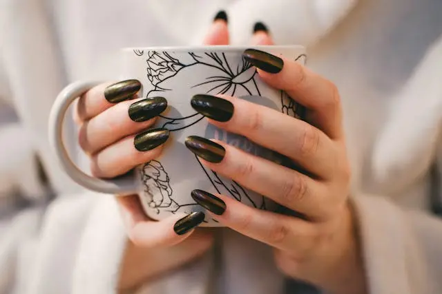 Deep olive green nails paired with a warm mug — autumn vibes, anytime.